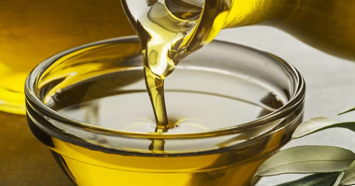 Golden carrier oils in clear glass bottles with almonds, coconut and jojoba seeds.